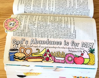 May include: A colorful bookmark with a variety of food illustrations, including a pretzel, hot dog, pizza, donut, and pineapple. The bookmark has the text "God's Abundance is for ME! But my God shall supply all your need according to his riches in glory by Christ Jesus. Philippians 4:19"
