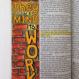 May include: A colorful, hand-drawn bookmark with the words "They had a MIND to WORK" in orange and yellow. The background is a brick wall design. The bookmark is placed on an open book.
