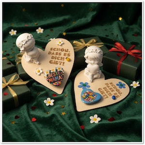 Op de afbeelding: Twee houten hartvormige plaquettes met de Duitse tekst "SCHÖN, DASS ES DICH GIBT!" en kleine engelenbeeldjes. Eén plaquette heeft een "BESTE MAMA!" magneet. De scène bevat verpakte cadeaus en decoratieve bloemen.