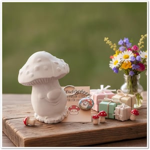Może przedstawiać: Biała ceramiczna figurka grzyba z uśmiechniętą buzią, brelok z ilustracją grzyba oraz kartka z napisem "Glück eine Portion Glück nur für dich". Trzy małe pudełka prezentowe i miniaturowe figurki grzybów z czerwonymi kapeluszami.