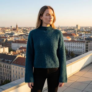 Puede incluir: Un suéter de color verde azulado con cuello alto y mangas largas. El suéter se combina con pantalones negros. El fondo presenta un paisaje urbano con edificios y un cielo despejado.