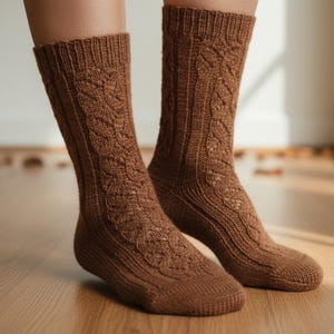 以下が含まれることがあります： ケーブル編みの模様が入った茶色のニットソックス。暖かくアースカラーで、柔らかく質感のある糸で編まれているようです。木製の床に置かれています。