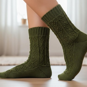 Könnte beinhalten: Ein Paar olivgrüne Strickstrümpfe mit Zopf- und Rautenmustern. Die Socken sind kniehoch und haben gerippte Bündchen. Das Bild zeigt die Socken an den Füßen einer Person, wobei die detaillierte Strickarbeit und die Farbe der Socken im Vordergrund stehen.