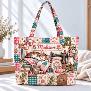 Könnte beinhalten: Eine gesteppte Tragetasche mit einem Patchwork-Blumenmuster in Rot, Grün und Weiß. Die Vorderseite zeigt eine schlafende getigerte Katze, eine Vintage-Nähmaschine, Garnrollen, eine Schere und ein Glas mit Knöpfen sowie den Namen Madison.