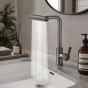 May include: A contemporary brushed steel tap with water cascading into a white sink. The tap features a rectangular spout and a single lever handle. A soap bottle and a tray with towels and a diffuser are in the background.