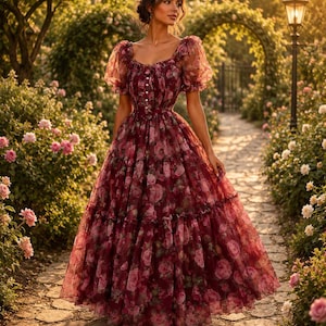 May include: A floor-length dress in a deep burgundy hue featuring a sheer, layered tulle overlay with a repeating pink rose floral print. The garment has short, puffed sleeves, a square neckline, and a row of small buttons down the centre bodice.