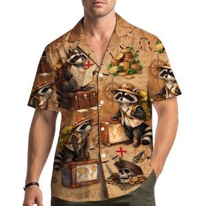May include: A short-sleeved button-down shirt featuring a repeating pattern of raccoons dressed as explorers on a treasure map background. The raccoons are depicted with hats, backpacks, and suitcases, with a skull and treasure chest graphic.