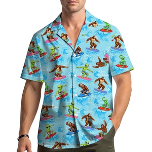 Puede incluir: Camisa azul claro con botones y un patrón repetido de extraterrestres y figuras de Pie Grande surfeando. La camisa de manga corta presenta un cuello clásico y cierre de botones. El diseño incluye olas azules y tablas de surf coloridas.