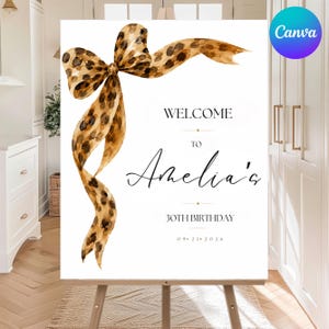 May include: A white rectangular birthday welcome sign featuring a large watercolor leopard print bow in the upper left corner. The text reads: WELCOME TO Amelia's 30TH BIRTHDAY 09 21 2026. The sign is displayed on a wooden easel stand.