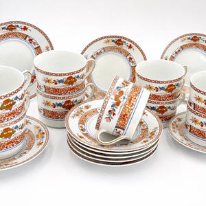 Peut inclure: Service à thé en porcelaine complet avec tasses, soucoupes et assiettes blanches. L'ensemble est décoré d'un motif répété de motifs floraux orange, bleus et jaunes. Les tasses ont des anses et les assiettes sont rondes.