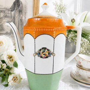 Peut inclure: Une cafetière en porcelaine avec un corps blanc, une section supérieure orange vif et une base vert clair. Elle possède un couvercle haut avec un bouton blanc, une anse courbée et un bec verseur. Un médaillon ovale central présente un motif floral.