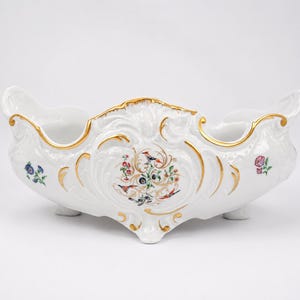 May include: White porcelain decorative bowl with gold trim and floral and bird motifs. The bowl has a scalloped edge and is supported by three small feet. The design includes colorful birds and flowers.