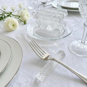 Peut inclure: Un ensemble de porte-couteaux en verre transparent avec un motif géométrique taillé en diamant. Chaque pièce rectangulaire présente des bords facettés qui captent la lumière. Un porte-couteau est placé sous une fourchette en argent.