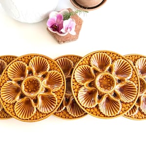 Peut inclure: Ensemble de six assiettes à huîtres en céramique. Chaque assiette présente un puits central et six compartiments en forme de coquillage, le tout dans un glaçage brun chaud. Les assiettes ont une bordure en forme de panier tressé.
