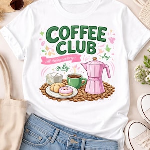 May include: White t-shirt with a colorful graphic that says "COFFEE CLUB" in green letters. The graphic includes a pink coffee maker, a green mug, and a plate of pastries. The shirt is paired with blue jeans and white sneakers.