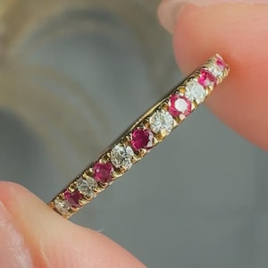 May include: A thin gold band ring featuring an alternating pattern of round-cut red rubies and clear white diamonds set in a row. The gemstones are securely held in place by small metal prongs along the entire visible length of the jewellery piece.