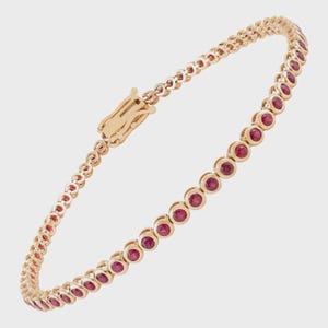 Op de afbeelding: Een roségouden tennisarmband met een doorlopende rij ronde, in een chaton gezette rode robijnen. De armband is opgebouwd uit individuele ronde metalen zettingen voor elke edelsteen en bevat een veilig, geïntegreerd bakslotmechanisme.