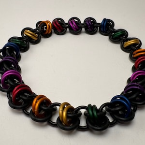 May include: A rainbow coloured chainmail bracelet with black links and colourful metal rings. The bracelet is made of metal and has a circular shape.