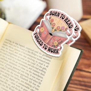 May include: A pink sticker with the text "BORN TO READ" and "FORCED TO WORK" over an open book. The sticker features a floral design with smiling flowers and a ribbon banner.