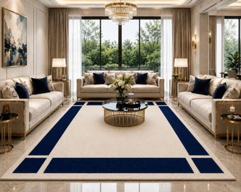 May include: A rectangular area rug featuring a cream-coloured centre field framed by a bold navy blue border with geometric corner accents. The rug is positioned on a polished floor in a living room setting with cream sofas and a glass coffee table.
