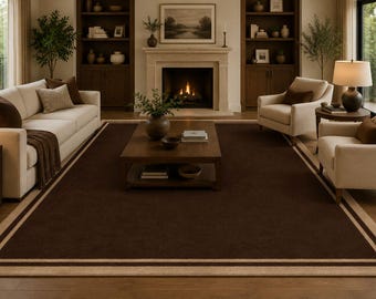 May include: A living room with a dark brown rectangular rug, featuring a light beige border. The room includes a white sofa, two armchairs, a wooden coffee table, a fireplace, and built-in bookshelves. The room is well-lit with natural light.