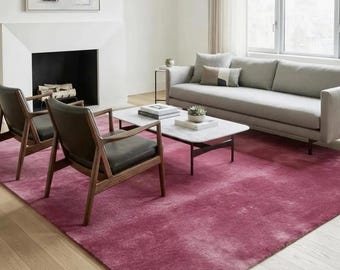 May include: A large, rectangular area rug in a deep magenta hue with a subtle, mottled texture. The rug features a soft, plush pile and covers a significant portion of the light-coloured wooden floor, providing a bold colour contrast to the room.