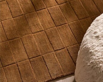May include: A rectangular area rug in a solid medium brown colour featuring a grid pattern of recessed lines that create a series of raised, uniform rectangular blocks across the entire surface of the soft, textured textile floor covering.