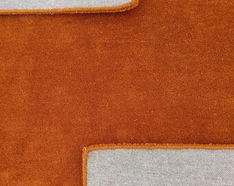 May include: A vibrant burnt orange rug with a soft, plush texture. The rug features two rectangular sections of light grey backing material visible at the top and bottom corners, showing the underside construction and orange stitched edges.