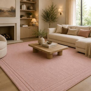 Puede incluir: Salón con una gran alfombra rosa claro. Un sofá seccional beige con cojines está a la derecha. También hay una mesa de centro de madera y un sillón cómodo. La habitación tiene una paleta de colores neutros.
