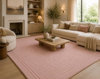 May include: A living room with a large, pale pink rug. A beige sectional sofa with cushions is on the right. A wooden coffee table and a comfortable armchair are also present. The room has a neutral colour palette, with a painting and a fireplace.