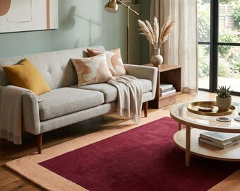 May include: A living room with a grey sofa, cushions, and a throw. A burgundy and beige rug is on the wooden floor. A round coffee table and a floor lamp are also present, creating a cozy atmosphere.
