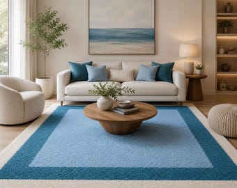 May include: A living room with a light blue and cream rug with a dark blue border. A cream sofa with blue cushions is in front of a seascape painting. A round wooden coffee table and a white armchair complete the scene. The rug is approximately 200cm x 300cm.