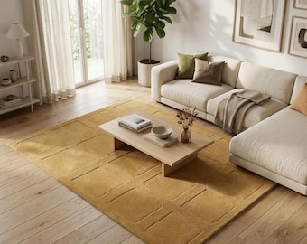 May include: A rectangular area rug in a solid mustard yellow colour featuring a raised geometric square pattern. The rug is placed on a light-toned wooden floor in a living room setting, positioned beneath a low wooden coffee table.