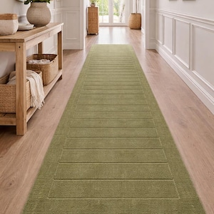 Puede incluir: Una alfombra larga de pasillo verde oliva con un dise&ntilde;o rectangular. La alfombra presenta una superficie texturizada con l&iacute;neas horizontales, creando un patr&oacute;n sutil. Est&aacute; colocada sobre un suelo de madera en un pasillo bien iluminado.