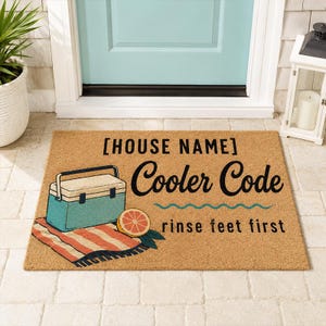 Pode incluir: Um tapete retangular com o texto "[NOME DA CASA] Cooler Code rinse feet first". O tapete apresenta uma geleira turquesa, uma toalha listrada e uma ilustração de fatia de toranja.