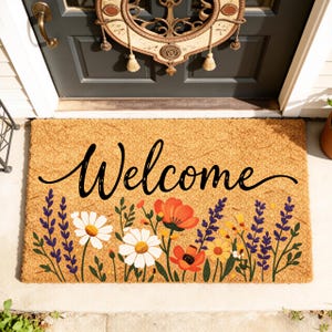 Può includere: Un zerbino rettangolare in fibra di cocco con la scritta "Welcome" in nero. La parte inferiore del tappeto presenta un motivo floreale con margherite bianche, papaveri arancioni, fiori gialli e lavanda viola su sfondo beige.