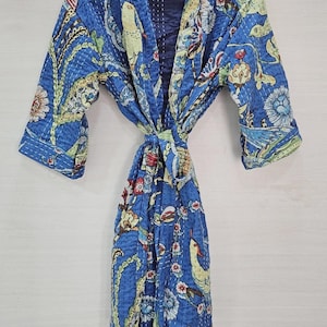 Peut inclure: Robe bleue à motifs avec un motif floral et d'oiseaux. La robe est faite d'un tissu matelassé et possède une fermeture à nouer. Les manches sont aux trois quarts. La robe est suspendue à un cintre en bois.