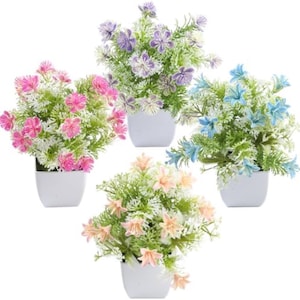May include: Four small artificial flower arrangements in white square pots. The flowers are pink, purple, blue, and peach, with green and white foliage. These decorative plants are suitable for home or office decor.