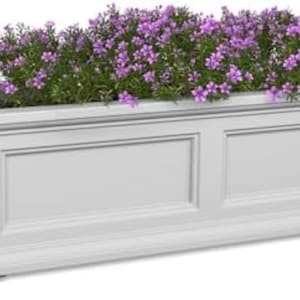 Könnte beinhalten: Eine weiße, rechteckige Pflanzkasten mit leuchtend lila Blumen gefüllt. Der Pflanzkasten hat ein klassisches Design mit Paneeldetails und einem dekorativen Sockel, ideal für die Außendekoration.