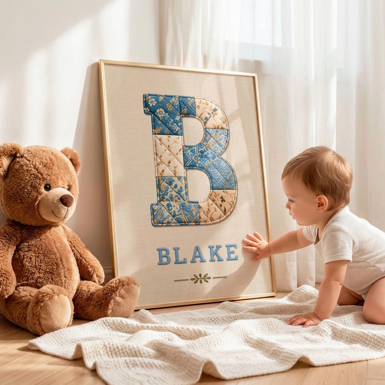 May include: A framed wall art piece featuring a large, quilted letter B in blue and beige floral patterns, with the name BLAKE printed in blue below it, accompanied by a small decorative floral icon centered at the bottom of the beige canvas.