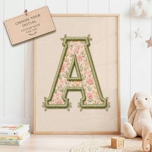 May include: A framed wall art print featuring a large letter A with a floral pattern in shades of pink, orange, and green. The letter is outlined with a thick, textured green embroidered border. A small tag reads: CHOOSE YOUR INITIAL CUSTOM MADE FOR YOU.