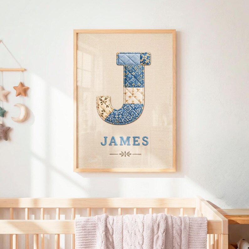 May include: A framed wall art print featuring a large letter J with a blue and cream quilted patchwork pattern. Below the letter, the name JAMES is printed in blue capital letters, followed by a small decorative horizontal line and floral icon.