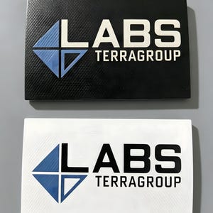 Könnte beinhalten: Zwei rechteckige Schilder mit dem Text LABS TERRAGROUP und einem rautenförmigen Logo. Das obere Schild ist schwarz mit weißem Text und einer blauen Raute. Das untere Schild ist weiß mit schwarzem Text und einer blauen Raute.