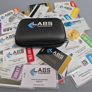 Puede incluir: Un estuche de transporte negro con cremallera y el logotipo de Labs TerraGroup se encuentra sobre una colección de varias tarjetas de identificación de seguridad de plástico. Las tarjetas presentan etiquetas de área codificadas por colores, incluyendo rojo, azul, verde y violeta, junto con el logotipo y texto de Labs TerraGroup.