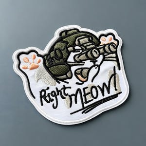 Op de afbeelding: Een geborduurde patch met een kat die een tactische helm met nachtkijker draagt. De kat heeft lichtoranje pootafdrukken en de tekst Right MEOW! is in zwart garen geborduurd op een witte achtergrond met een witte rand.