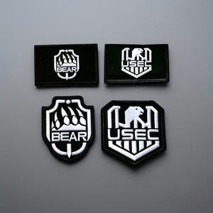 May include: Four black and white embroidered patches featuring military-style logos. Two rectangular patches and two shield-shaped patches display the text BEAR with a claw graphic and the text USEC with a stylized eagle graphic in white thread.