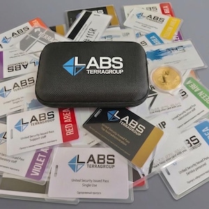 May include: A black textured rectangular carrying case with the white and blue Labs Terragroup logo sits atop a collection of various plastic security identification badges, each featuring the same logo and specific area access labels.