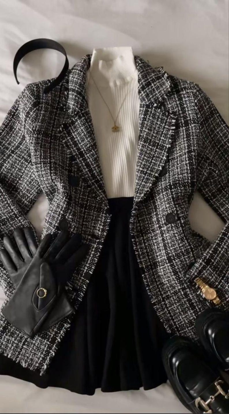 Op de afbeelding: Een zwart-witte tweed blazer met een dubbele rij knopen, gedragen over een witte geribbelde top met opstaande kraag. Accessoires zijn een zwarte haarband, een gouden ketting met hanger, zwarte leren handschoenen met een gouden ring, een gouden horloge en zwarte loafers.