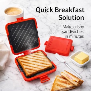 Könnte beinhalten: Ein roter Sandwichmaker mit schwarzer Grillfläche, geöffnet, um ein getoastetes Sandwich zu zeigen. Das Bild enthält eine Tasse Kaffee, eine Butterdose, einen Spatel und den Text "Quick Breakfast Solution."