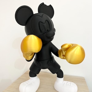 Puede incluir: Figura negra de Mickey Mouse con guantes de boxeo dorados y zapatos blancos. La figura tiene una mordida en una oreja. La figura est&aacute; en posici&oacute;n de boxeo.